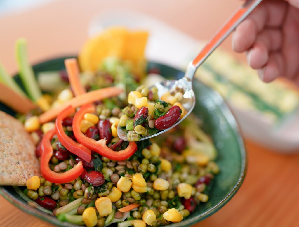 Spoonful of mixed bean and corn salad with red peppers, cucumber, carrots, and fresh herbs.